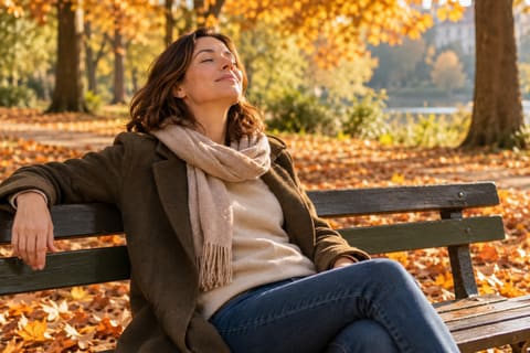 Femme assise sur un banc dans un parc en automne, les yeux fermés, qui respire calmement